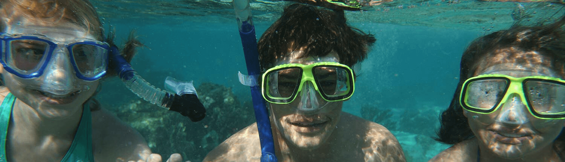 Three young people underwater in goggles and snorkeling gear mug at the camera.