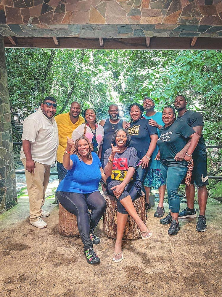 A joyful large family group poses under a stone arch in front of the jungle background.