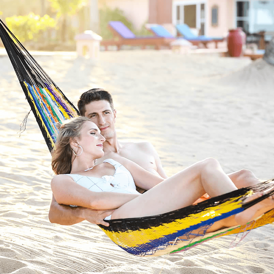 A blonde woman and a dark-haired man rest together in a colorful beach hammock on a sunny breezy day.