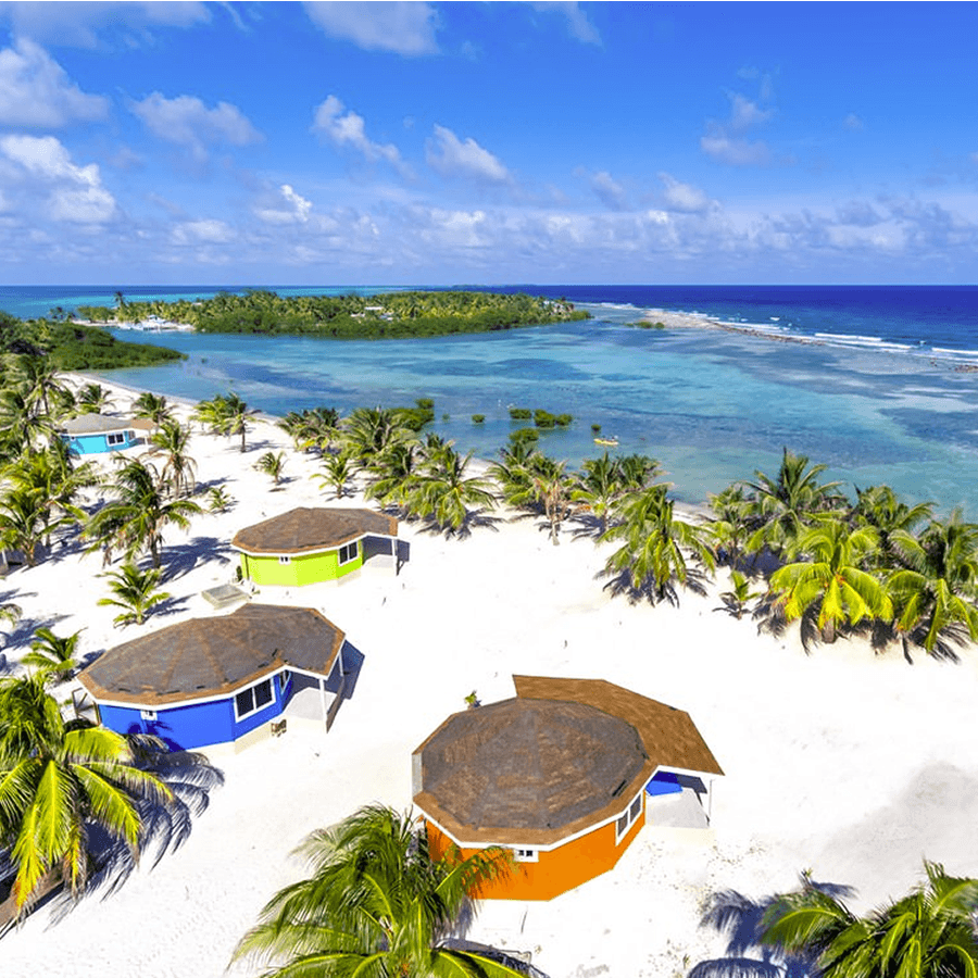 multi color yurts on beach with ocean, blue ski, palm trees and palm trees in surrounding area.