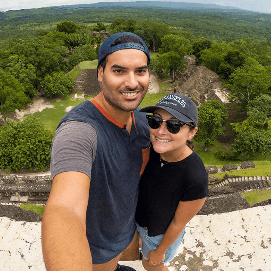 A happy young couple takes a selfie in front of expansive Mayan ruins.