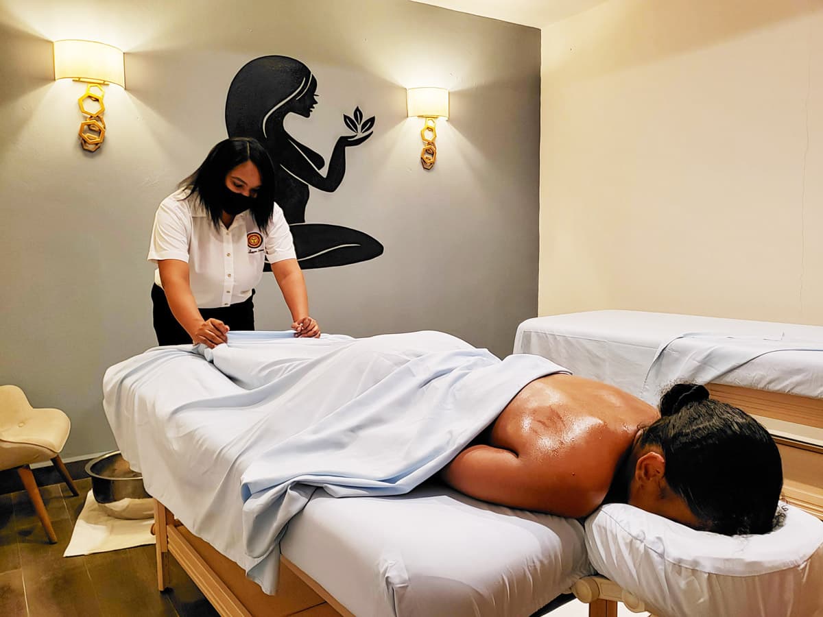 A massage therapist places a white sheet over a guest receiving a spa massage.