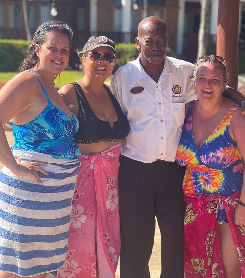 Four smiling individuals pose together outdoors, with a man in a white shirt standing in the middle and wearing a name tag.