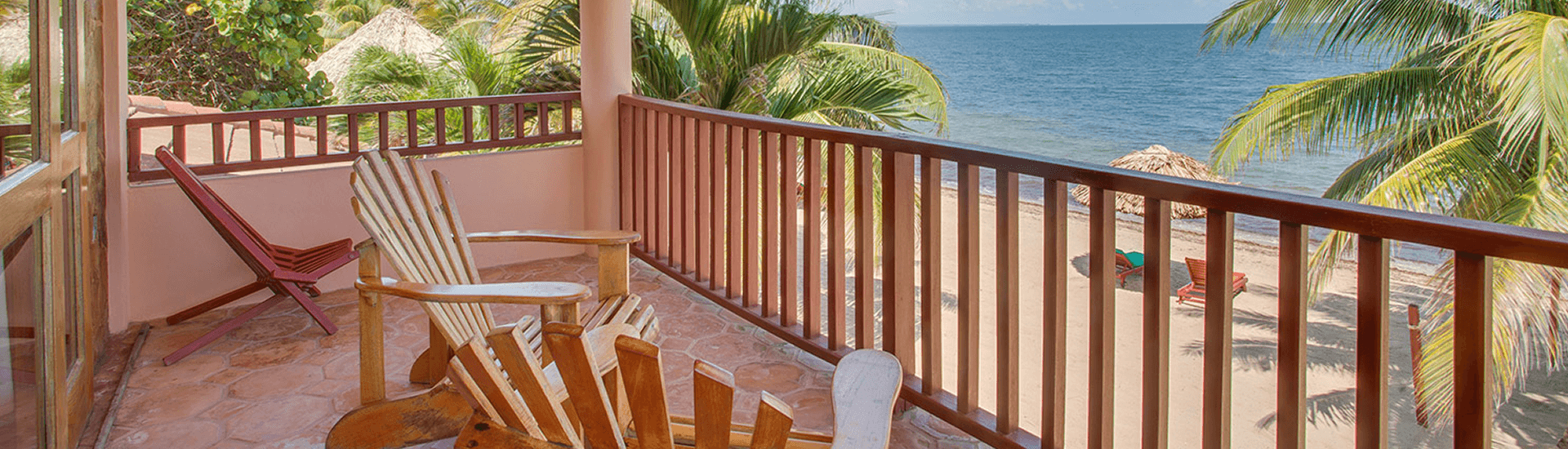 A balcony overlooking a beach with lounge chairs and a thatched-roof hut.