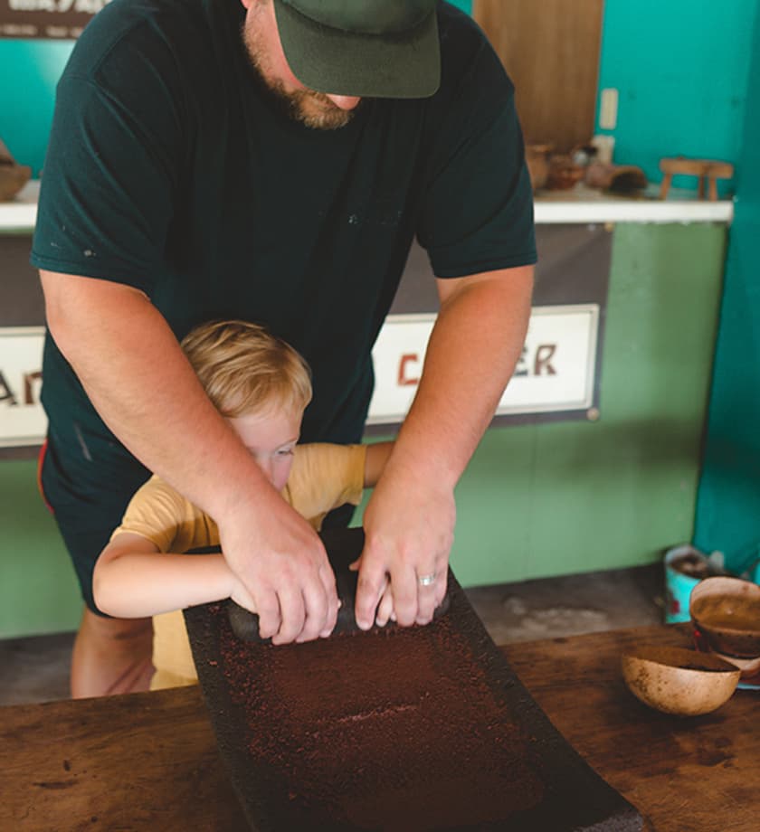 An adult and a child work together to grind ingredients on a flat surface.