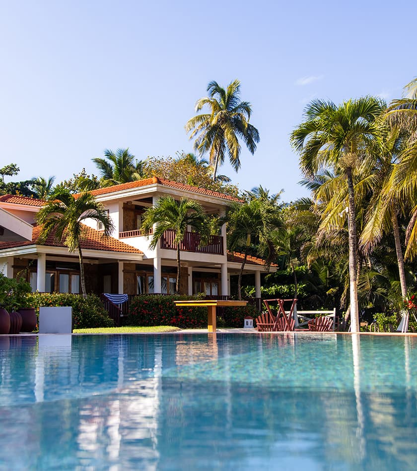 A luxurious villa surrounded by palm trees, reflecting in a tranquil swimming pool.