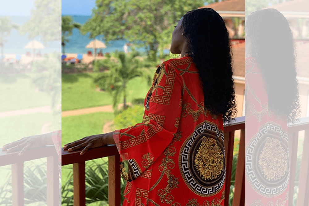 A young lady in an orange kimono gazes over the balcony of her villa to the ocean beach.