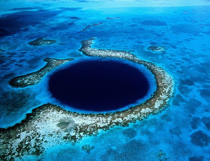 A breathtaking aerial view of the Great Blue Hole, a circular abyss surrounded by vibrant coral reefs in the Caribbean Sea.